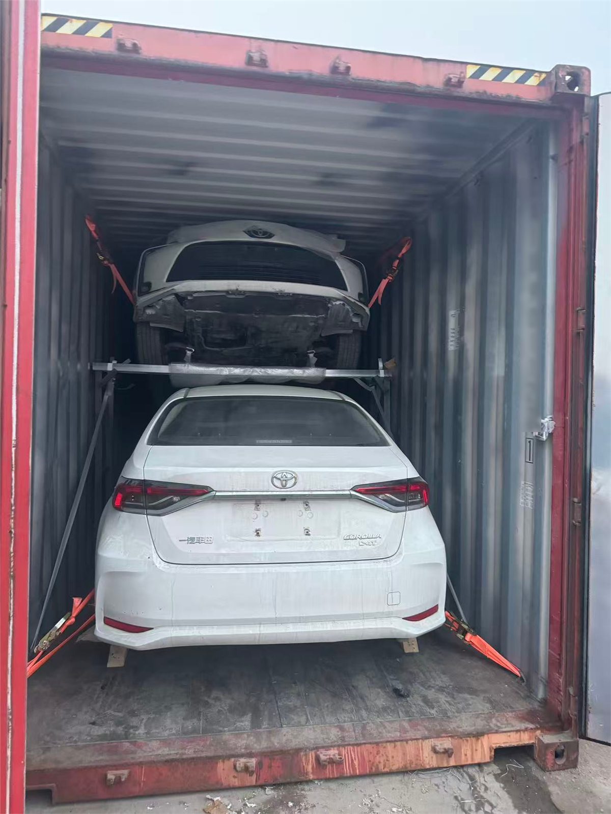 Vehicles loaded inside a shipping container with securing frame and straps